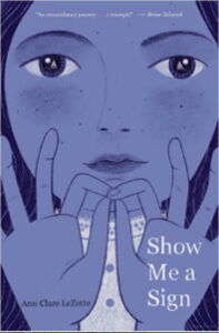 This book cover of Show Me a Sign, by Anne Clare LeZotte, features a sketched image of a young girl with serene eyes looking directly at readers. We see her hands signing the word “interpret.” There is a charcoal grey background, with the book title in white print. The girl’s face is in a bluish grey color. The Schneider Family Book Award stamp is also on the cover.