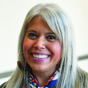 A smiling woman with long gray hair and hoop earrings.